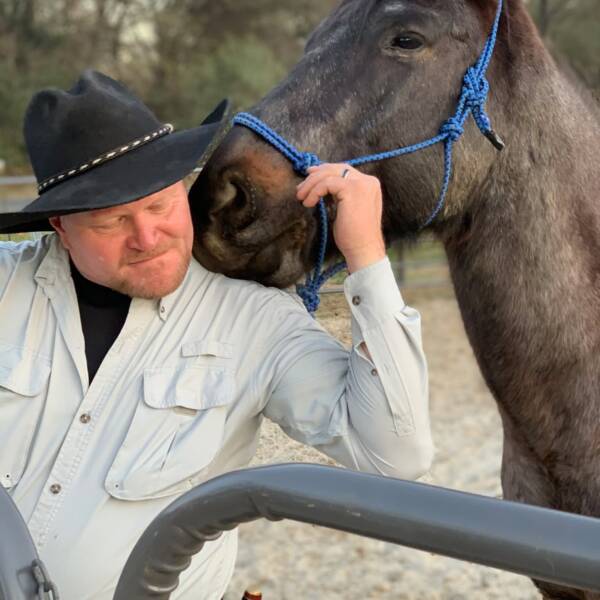 Man in black cowboy hat getting a friendly nudge from a horse standing behind him.